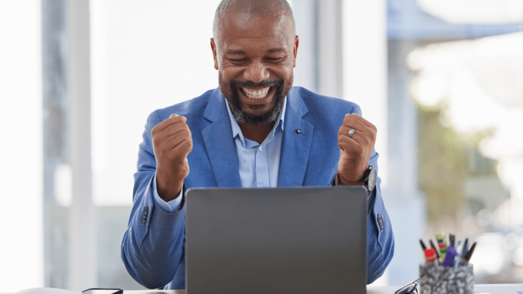 A person in a business suit is smiling while using a laptop