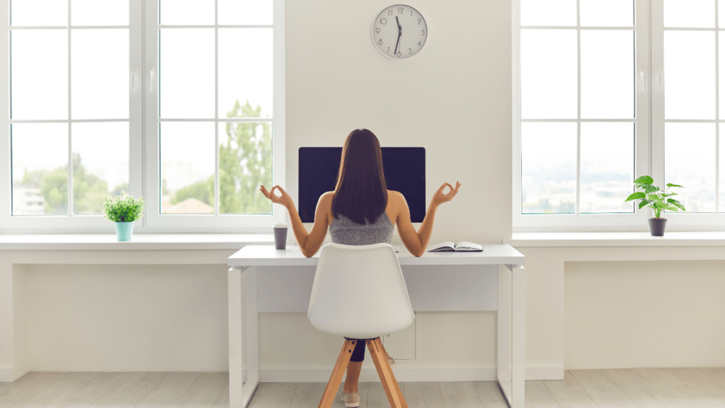 A person meditating on a yoga mat in front of a laptop