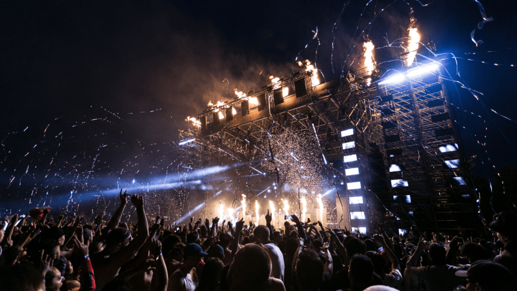 a crowd of people at a concert with fireworks in the background