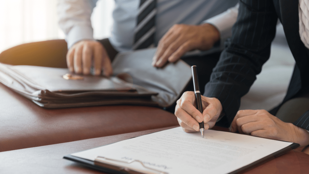 a person signing a contract with a pen and paper on a wooden table